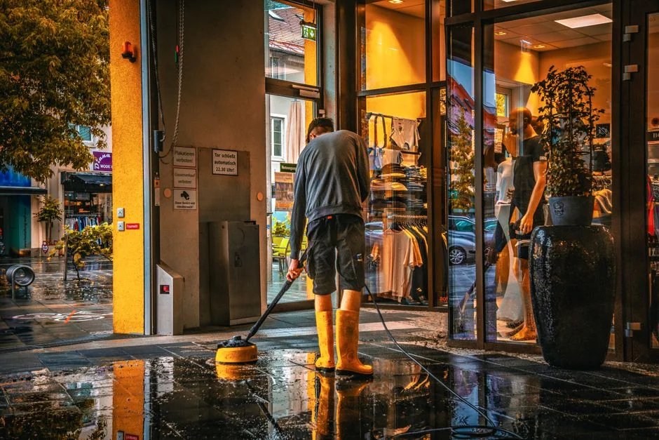 gallery-01 A man wearing a blue t-shirt cleaning a large glass pane indoors with a squeegee.